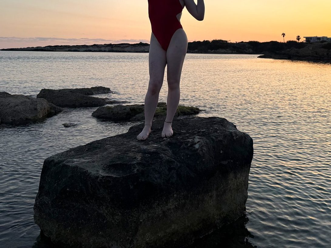 Lexi standing on a rock in the shallows at sundown, red swimsuit